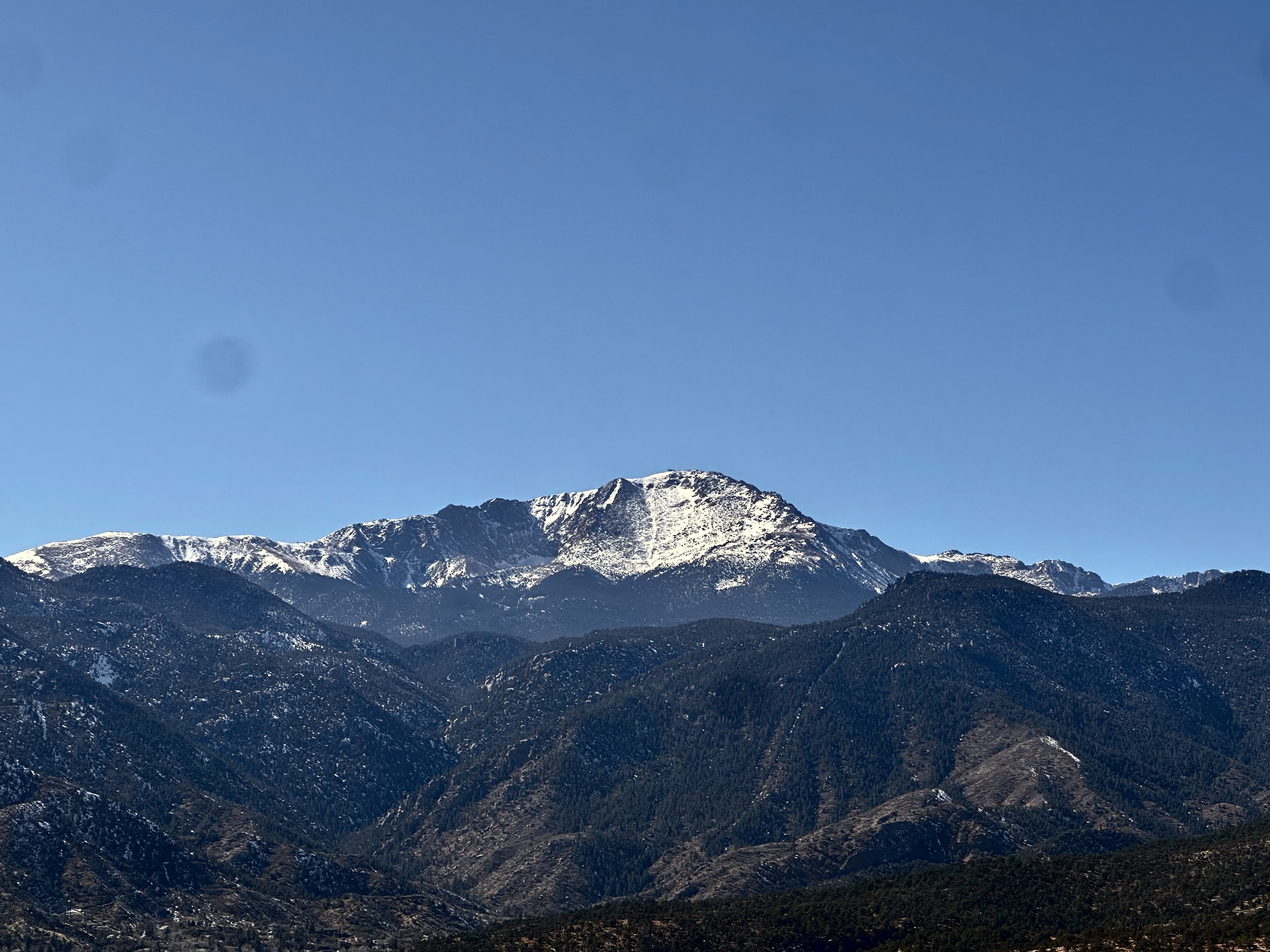 Pikes Peak under a deep blue sky, snow-capped and distant, calm and clear — the work bringing clarity
