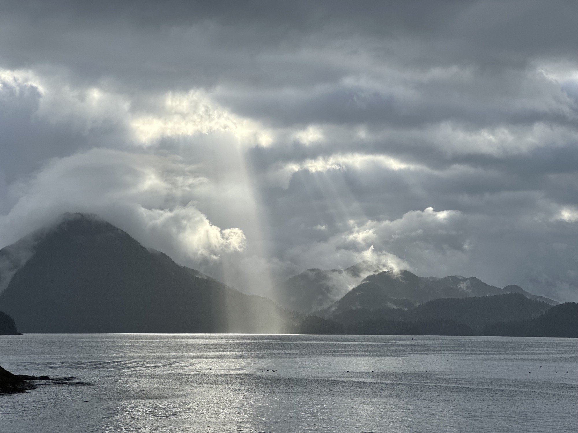 God rays breaking through storm clouds over Sitka mountains and water